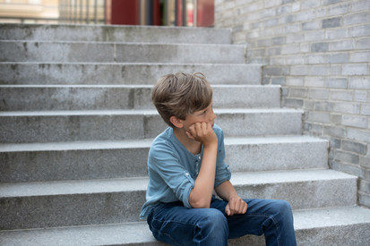 Ein kleiner Junge sitzt traurig auf einer Treppe