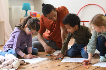 Symbolbild: Erzieher sitzt mit Kindern auf dem Boden und liest vor