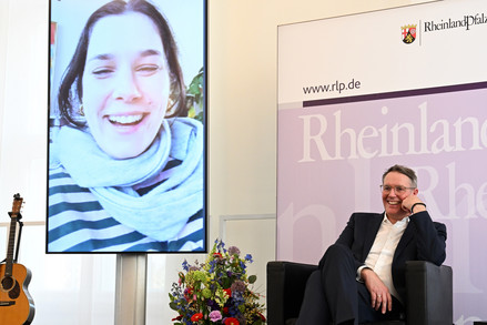 Preisträgerin Tara Louise Wittwer auf Bildschirm und Ministerpräsident Alexander Schweitzer bei der Preisverleihung des Marie Juchacz – Frauenpreis 2026