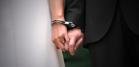Bildausschnitt: Hand von Braut und Bräutigam sind mit Handschellen aneinandergefesselt