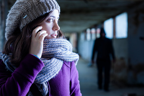 Eine Frau hält sich ein Handy ans Ohr - im Hintergrund ist schemenhaft eine Gestalt zu erkennen, die ihr folgt - Symbolbild für Notrufnummern und Hilfsangebote