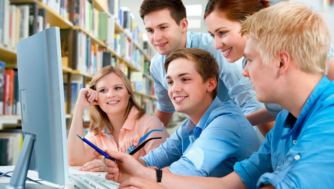 Foto: Fünf junge Menschen versammelt um einen Computerbildschirm - im Hintergrund befindet sich eine Bücherwand. Symbolbild für "Schulische Bildung"