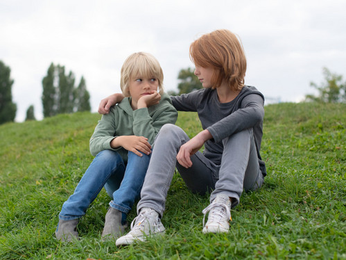 Symbolbild: Zwei traurige Kinder sitzen auf einer Wiese