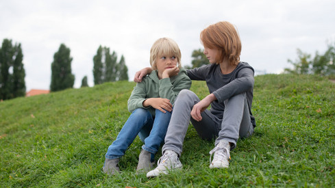 Symbolbild: Zwei traurige Kinder sitzen auf einer Wiese