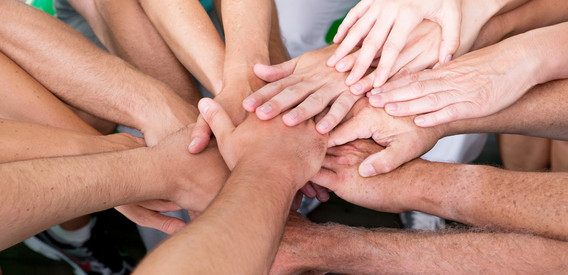 Menschen in unterschiedlichem Alter strecken ihre Arme aus und legen ihre Hände übereinander - Symbol für Zusammenhalt und Gemeinschaft