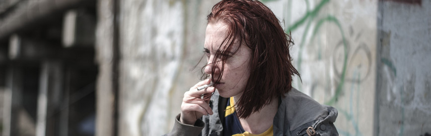 Bildausschnitt: Eine Frau mit verzweifeltem, resigniertem Blick zieht an einer Zigarette